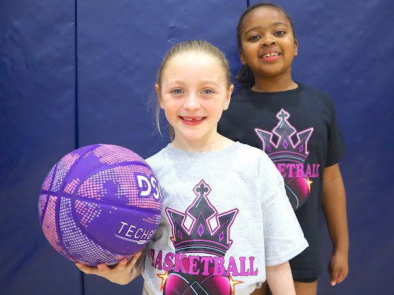 Two young girls smiling, one holding a purple basketball.