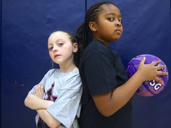 Two confident girls stand back-to-back, ready for basketball.